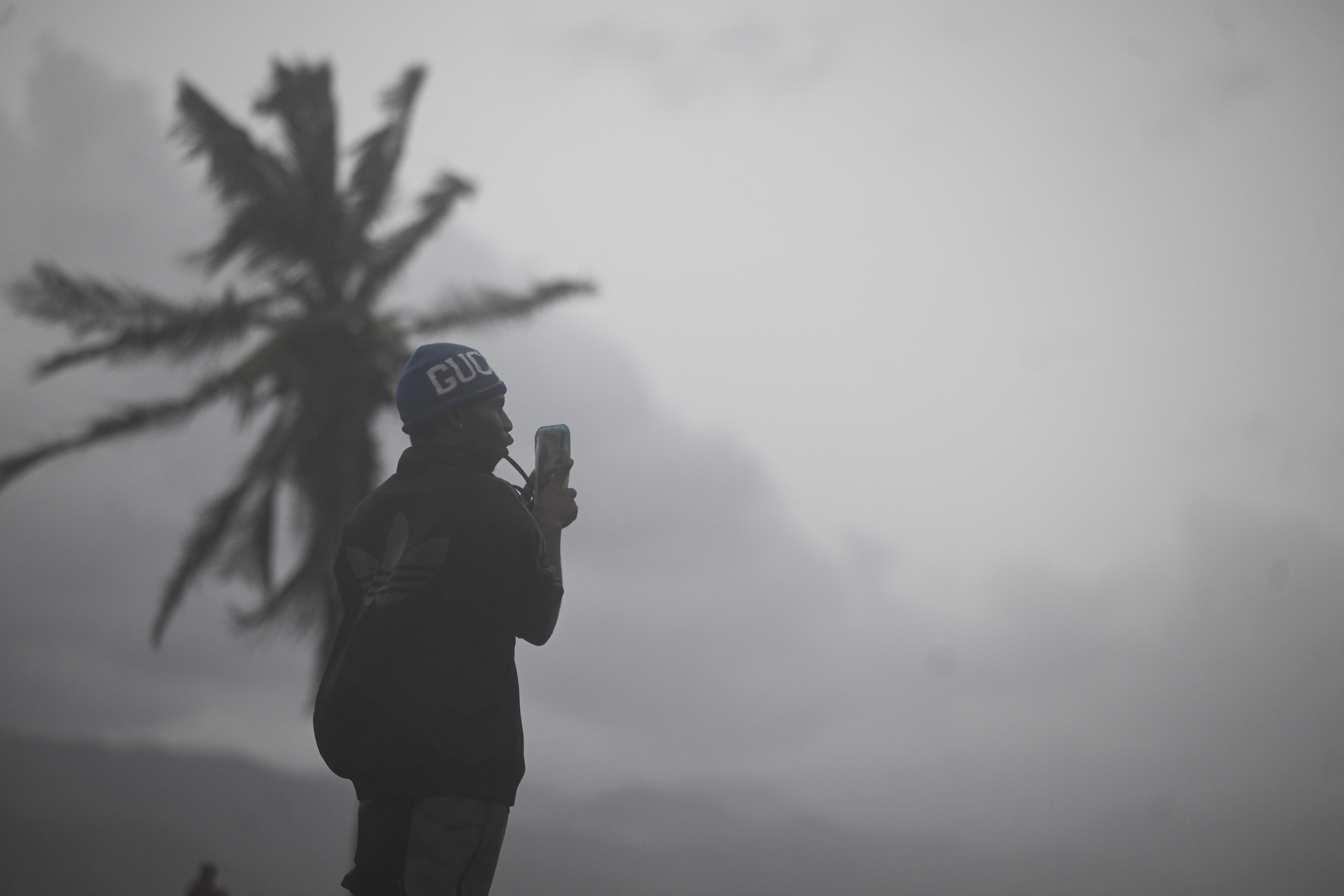 A man uses his cellphone at the waterfront in Kingston on October 27, 2025. Hurricane Melissa threatened Jamaica with potentially deadly rains after rapidly intensifying into a top-level Category 5 storm, as residents scrambled for shelter from what could be the island's most violent weather on record. Melissa has already been blamed for at least four deaths in Haiti and the Dominican Republic, and was set to unleash torrential rains on parts of Jamaica in a direct hit on the Caribbean island.